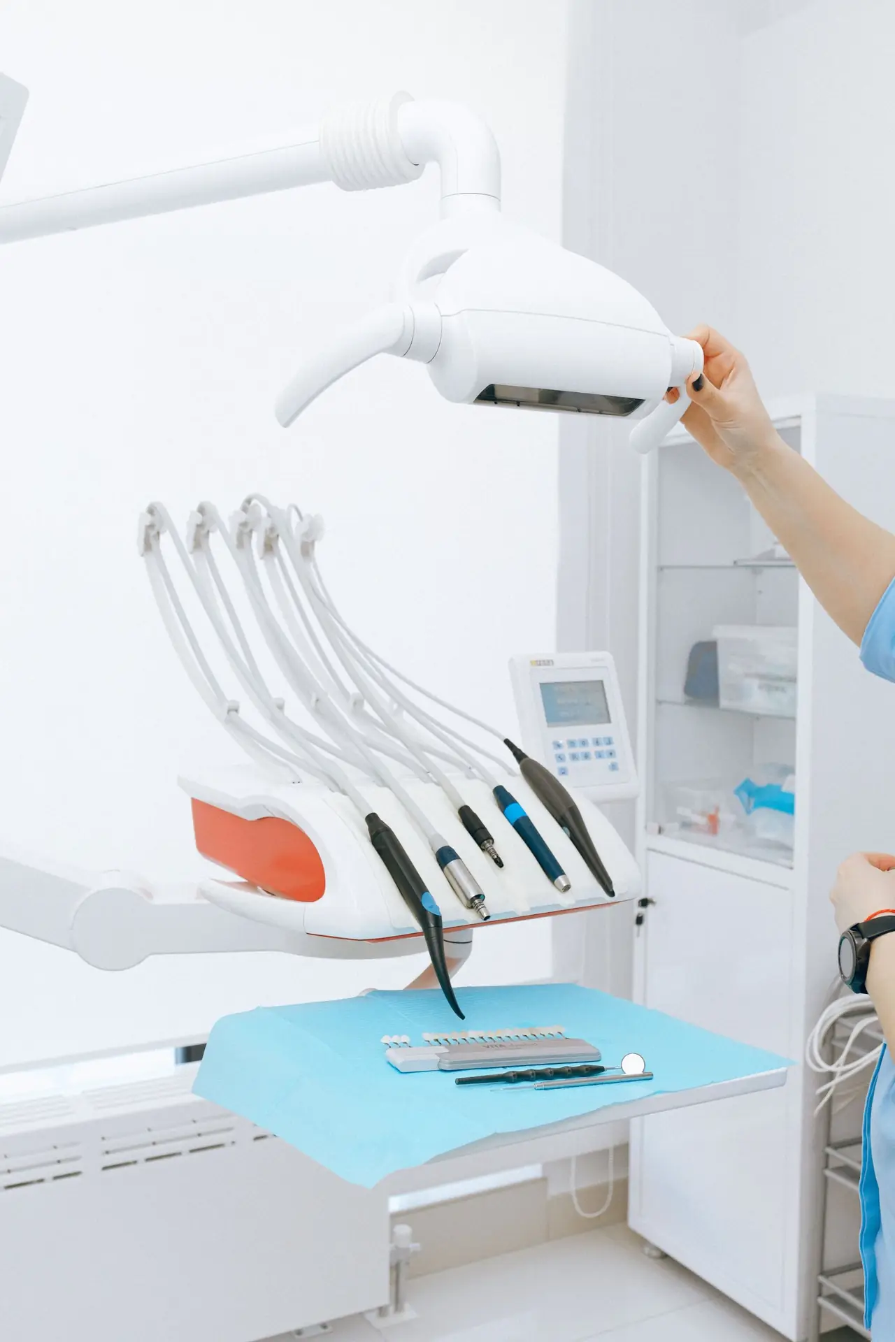Dentist adjusting the operating light above a delivery unit with handpieces and a shade guide