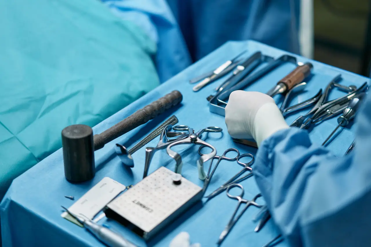 Surgical instrument tray with retractors, forceps, scissors and a mallet on blue drapes